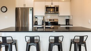 A modern kitchen with stainless steel appliances, a large island with bar stools, and pendant lighting. - Luxury. Steps to the Timberline Chairlift (Fernie)