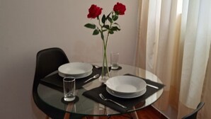 A dining table with two plates, a vase with red roses, and a glass of water.