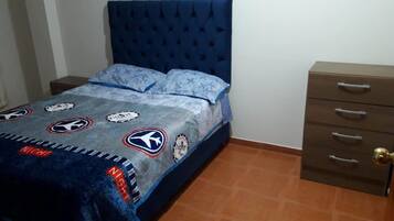 Una camera da letto con una testiera imbottita blu, un letto con copripiumino fantasia e un comodino in legno con cassetti.