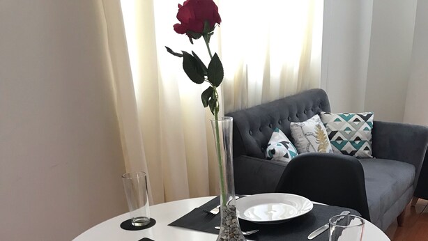 A dining table set with plates, cutlery, and a vase with a rose.