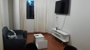 A small, sparsely furnished room with a single black sofa, a white side table, and a mounted TV.