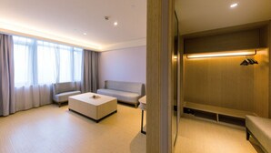 Moderni hotellihuone, jossa on vaaleanvärinen sohva, pieni sohvapöytä ja penkki.