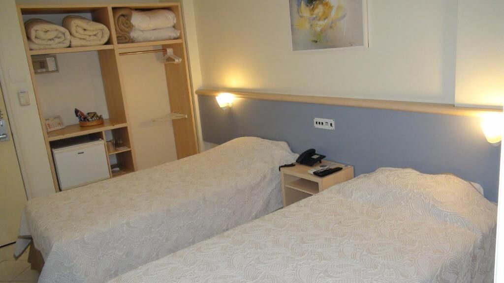 Et hotelværelse med to senge, et lille skrivebord med telefon og et skab med sammenfoldede håndklæder.