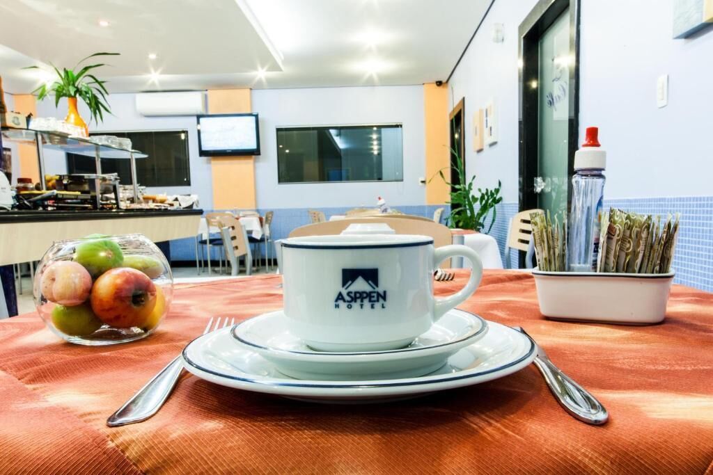 Morgenmad med en kop mærket 'Aspen Hotel' på et bord med en skål frugt og en vandflaske.