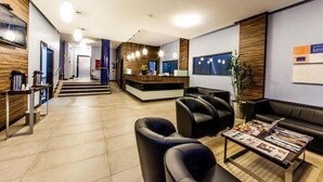 A modern reception area with a reception desk, seating area, and a staircase leading to other floors. - Asppen (Chapecó)