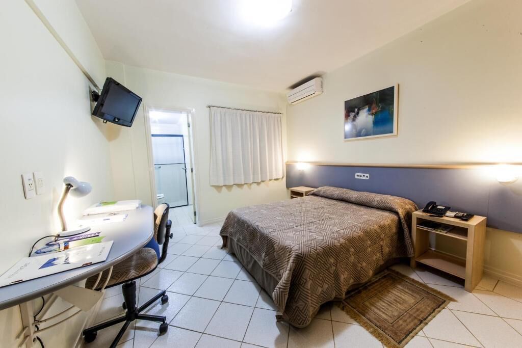 A hotel room with a bed, desk, chair, and a television mounted on the wall.