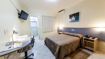 A hotel room with a bed, desk, chair, and a television mounted on the wall.