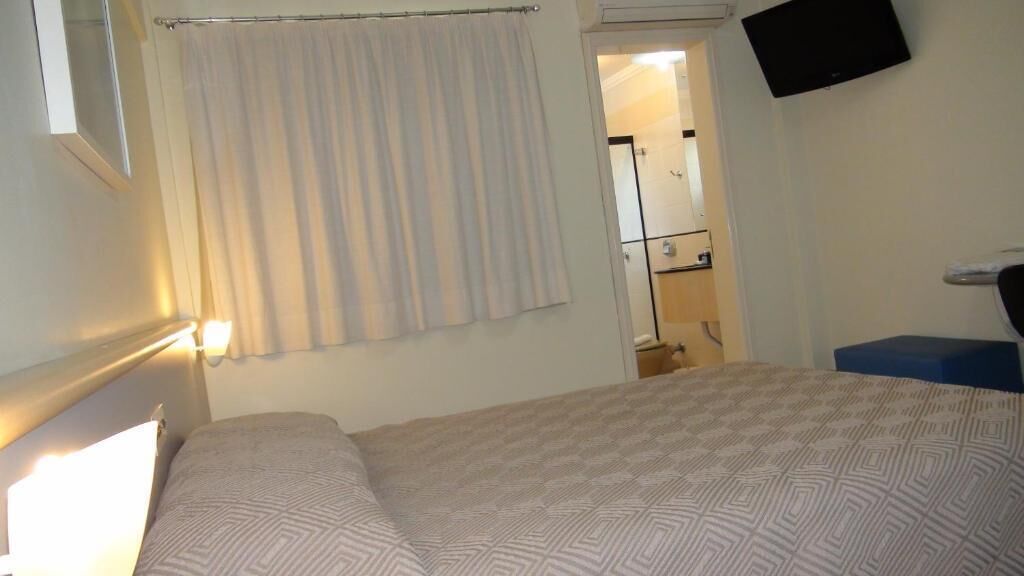 A hotel room with a bed, a television mounted on the wall, and a bathroom visible through an open door.