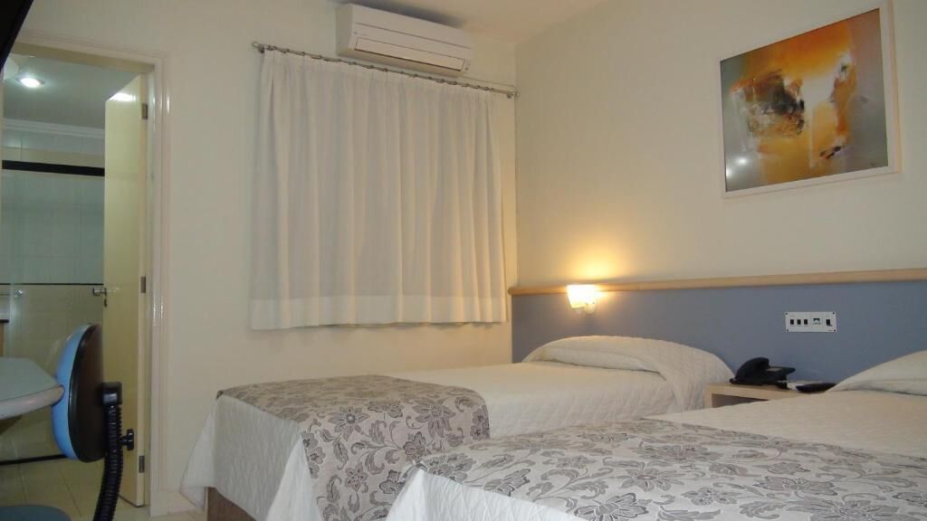 A hotel room with two beds, a bathroom with a shower, and a painting on the wall.