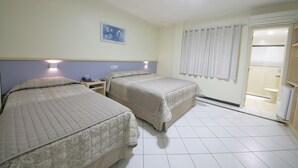 A hotel room with two beds, a nightstand, a wall-mounted phone, a painting, and a bathroom visible through a door. - Asppen (Chapecó)