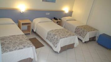 Habitación de hotel con tres camas individuales, cada una con mesita de noche y lámpara.