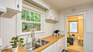 Eine Küche mit weißen Schränken, einer Holz Arbeitsplatte, einer Edelstahl-Spüle und einem Fenster mit Blick auf Grünflächen.