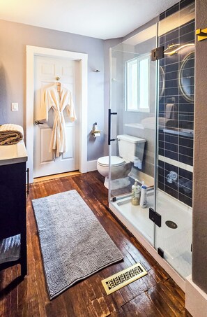 A modern bathroom with a glass shower enclosure, a white toilet, and a wooden floor.