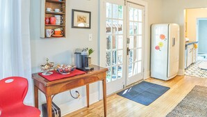 Una cocina con una mesa de madera, una silla roja, un refrigerador con motivos florales y una puerta que da a un balcón.