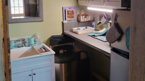 A compact kitchen with a sink, cabinets, a microwave, and a trash bin. - Cozy Tiny Cabin with a small porch and firepit. (Kempner)