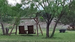 A swing set in a grassy area with trees and string lights. - Cozy Tiny Cabin with a small porch and firepit. (Kempner)