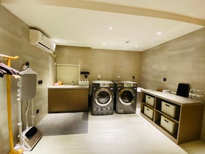 A modern laundry room with two front-loading washing machines, a sink, and a drying rack. - JI Hotel Shanghai The Bund Jiujiang Road (Shanghai)