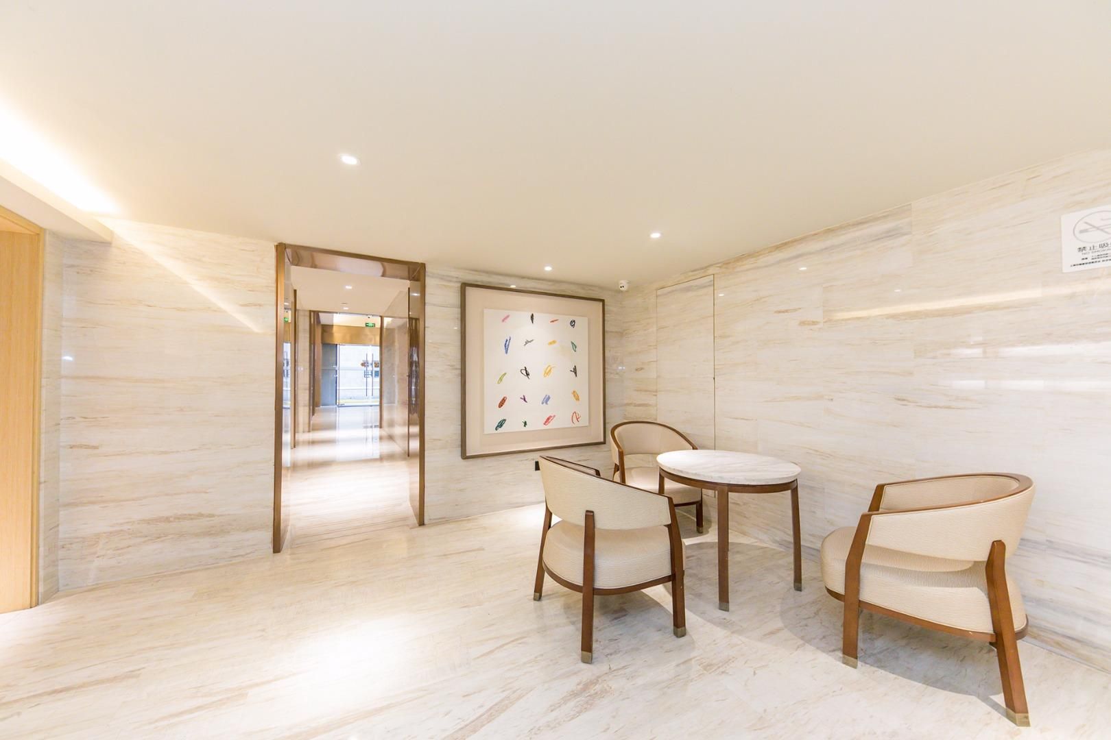 Un moderno vestíbulo de hotel con suelo de mármol, una mesa redonda con sillas y una obra de arte enmarcada en la pared.
