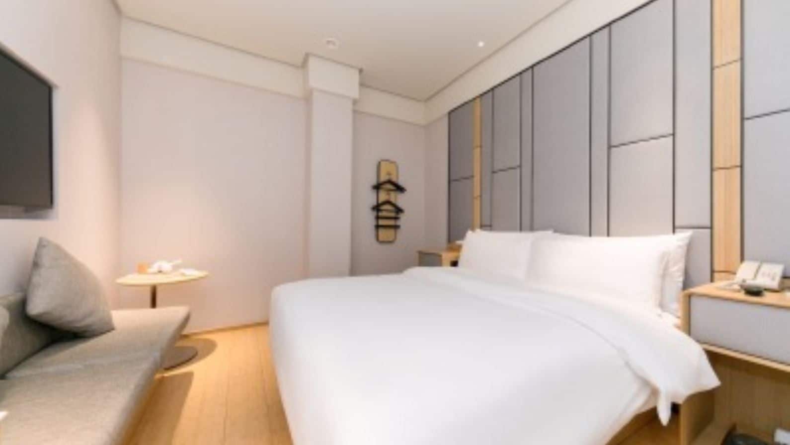 Una habitación de hotel moderna con una cama grande, una mesita de noche, una pequeña mesa redonda y un sofá.