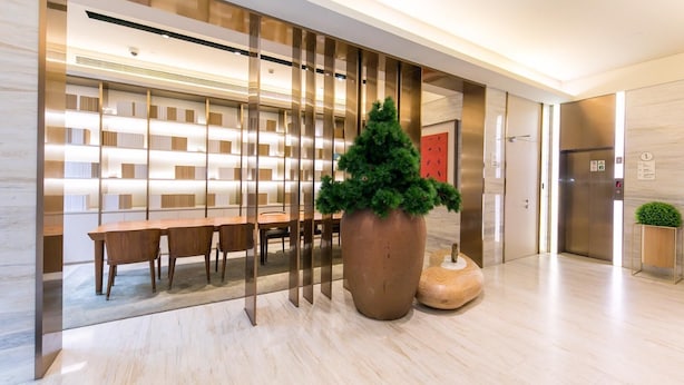 A modern lobby with a long reception desk, a large potted plant, and a wall-mounted bookshelf. - JI Hotel Shanghai The Bund Jiujiang Road (Shanghai)
