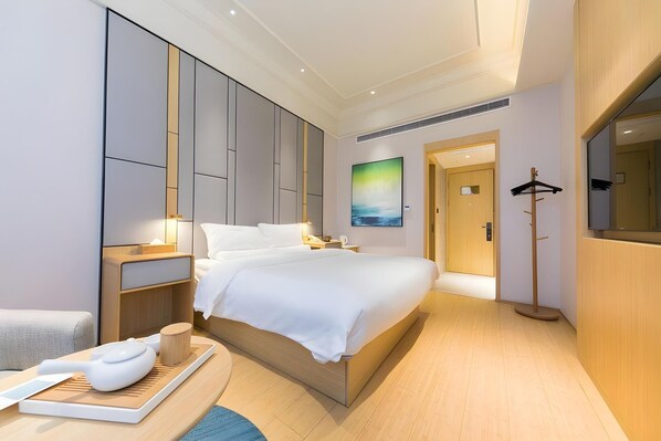 Un hotel moderno con una cama grande, mesitas de noche, suelo de madera y un cuadro en la pared.