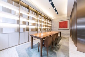 A modern conference room with a long wooden table, chairs, and a bookshelf with illuminated shelves. - JI Hotel Shanghai The Bund Jiujiang Road (Shanghai)