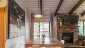 Uma sala de jantar com uma mesa e cadeiras de madeira, lareira de pedra e televisão na parede.