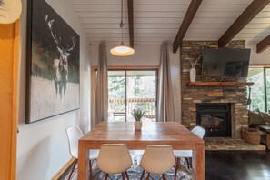 A dining area with a wooden table and chairs, a stone fireplace, and a mounted television. - Luxury 1+Loft Pet Friendly Mtn Retreat with Views! (Mammoth Lakes)
