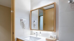A modern bathroom with a white sink, a large mirror, a hairdryer, and a wooden cabinet. - Ji Hotel (Shanghai)