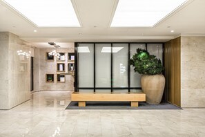 Un vestíbulo moderno con una recepción, una planta grande en maceta y un área de descanso.