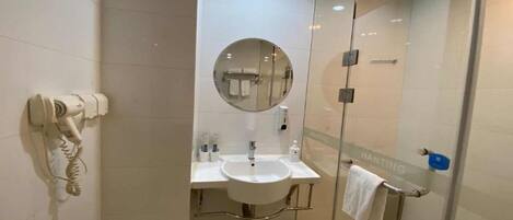 Um banheiro moderno com box de vidro, espelho redondo, pia com porta-toalhas e secador de cabelo na parede.