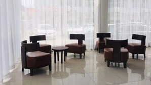 A room with a modern design, featuring a seating area with multiple chairs and a small table. The room has large windows with sheer curtains, allowing natural light to enter. - Hanting Hotel (Shenzhen)