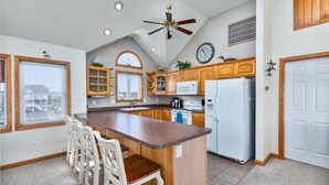 Une cuisine avec des meubles de rangement en bois, un îlot central doté de tabourets, un ventilateur de plafond et une grande fenêtre.