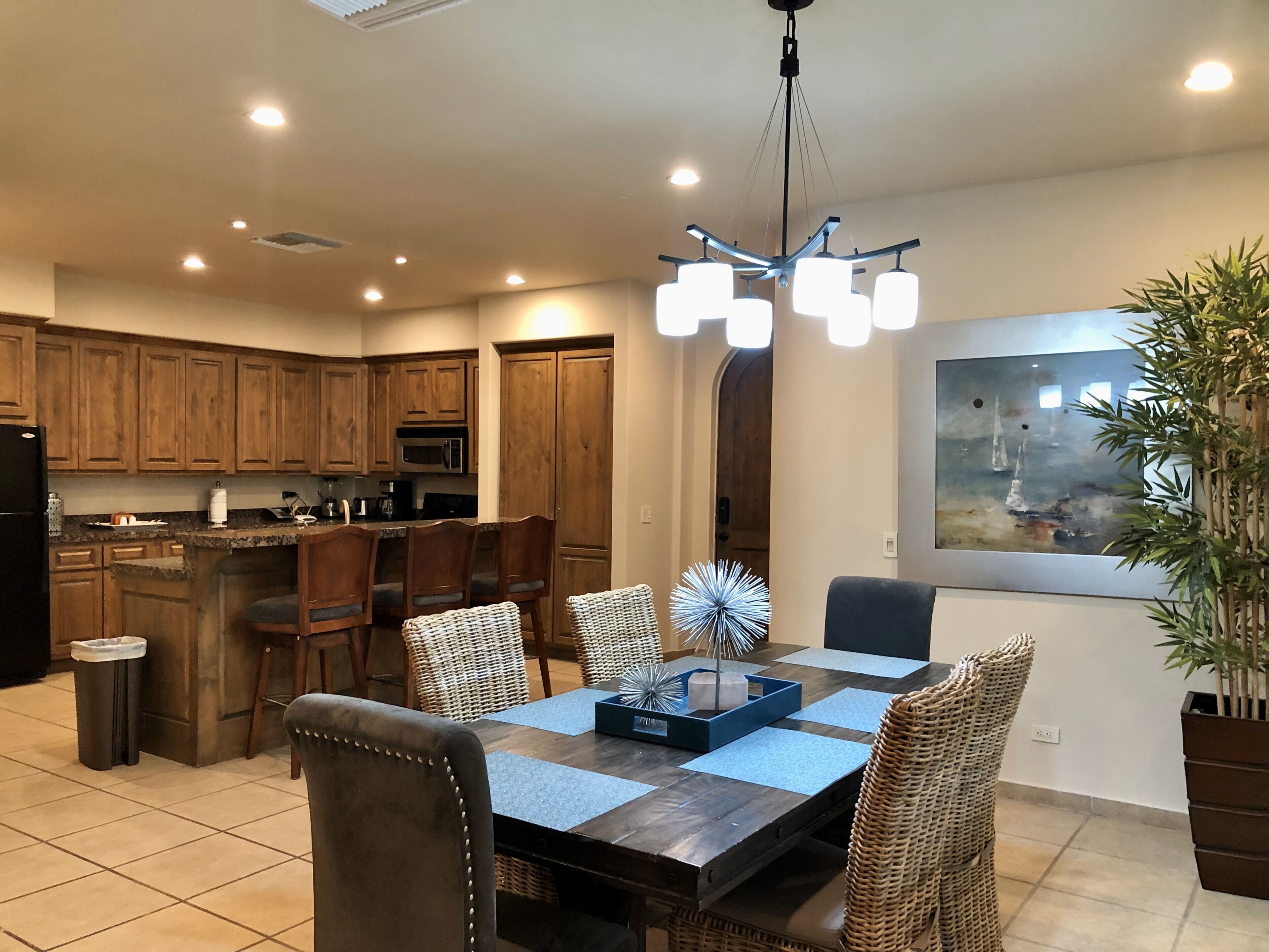 A modern kitchen with wooden cabinets, a central island with bar stools, and a dining table with chairs.