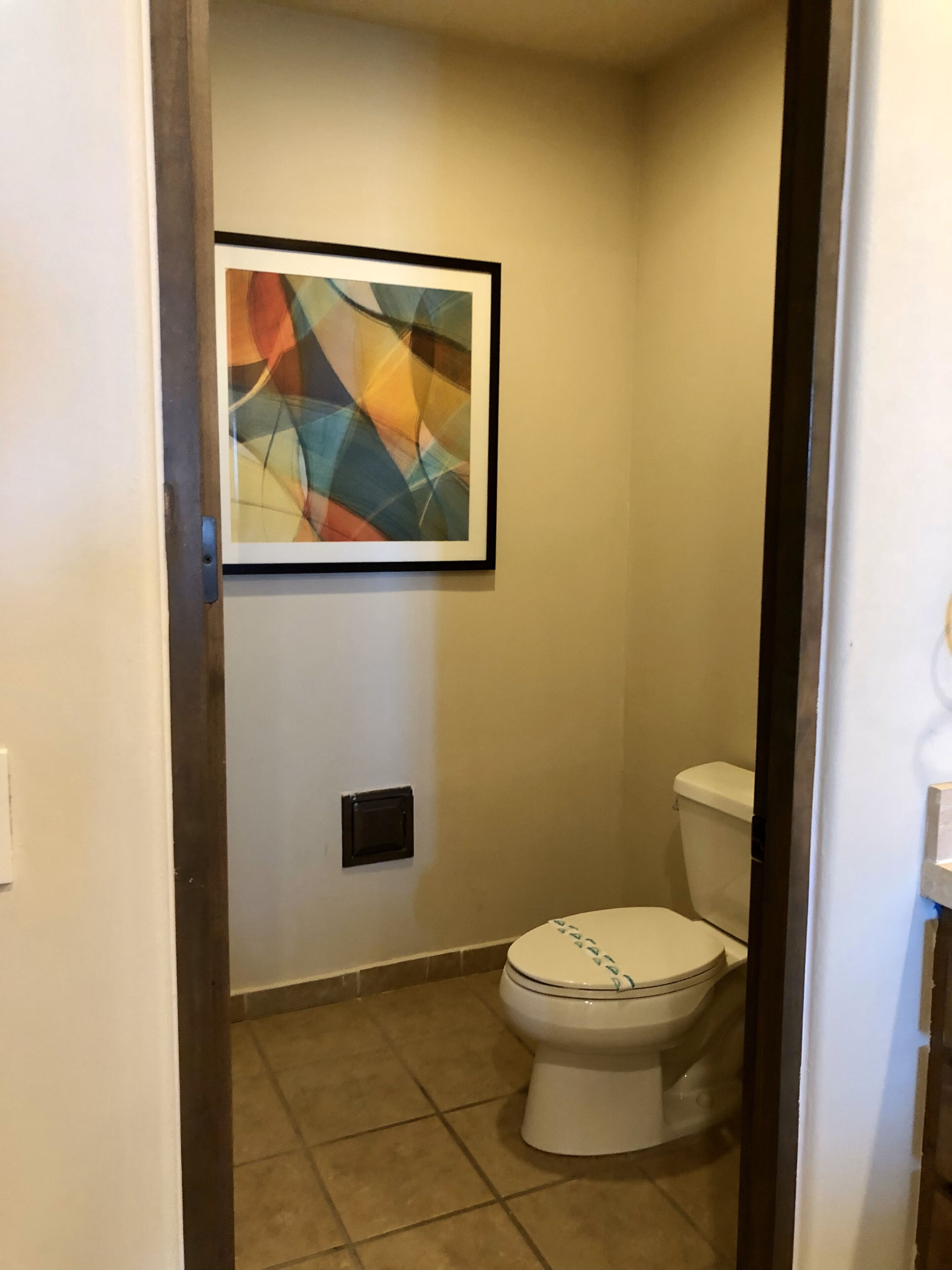 Un baño con inodoro, lavamanos empotrado en la pared y un cuadro abstracto enmarco.