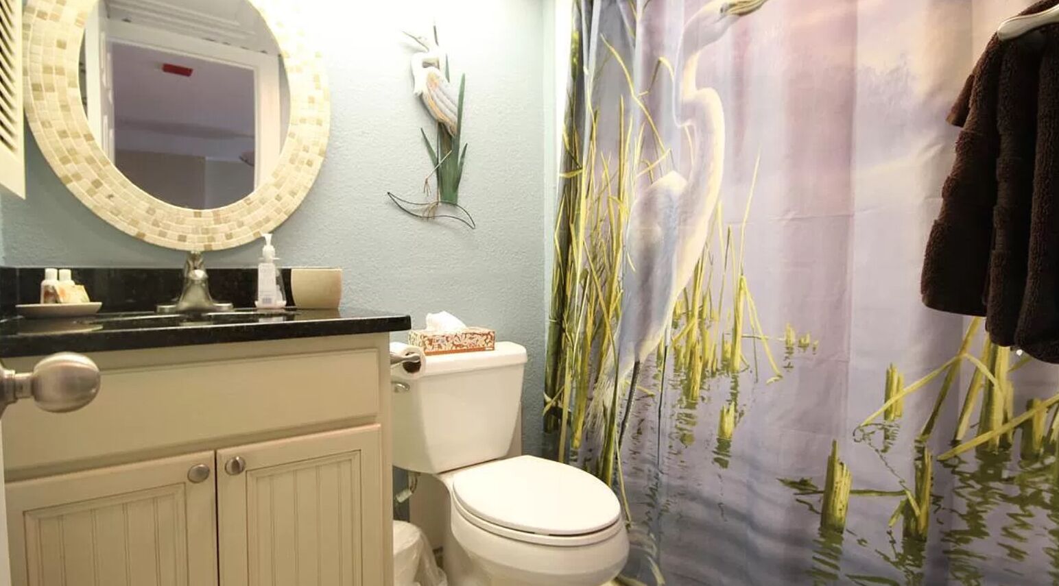 Un baño con inodoro, lavamanos con espejo y cortina de ducha con diseño natural.