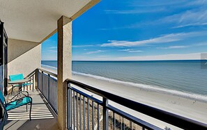 En balkon med udsigt over stranden, med gelænder og et par stole.