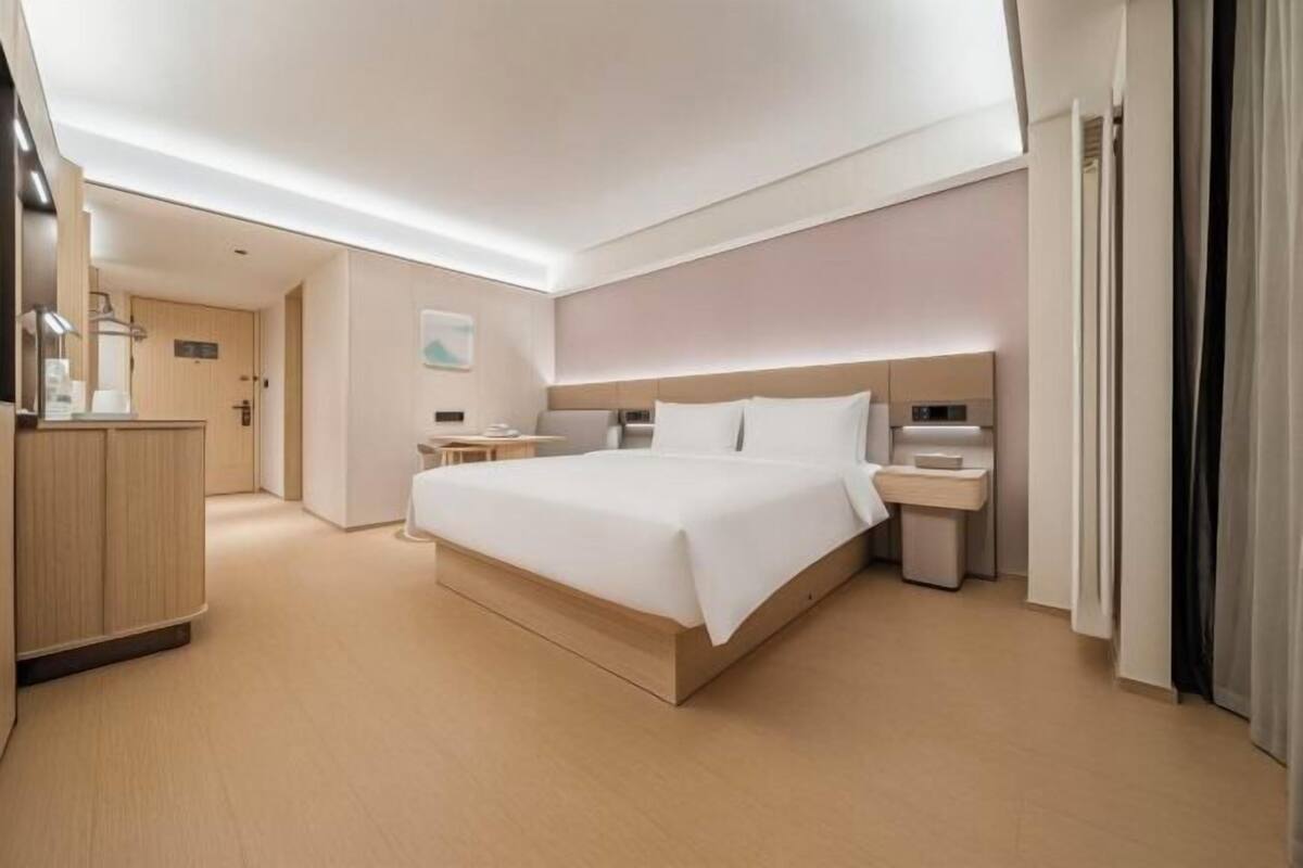 Una habitació d'hotel moderna amb un llit gran, taules de nit, un escriptori i un armari.