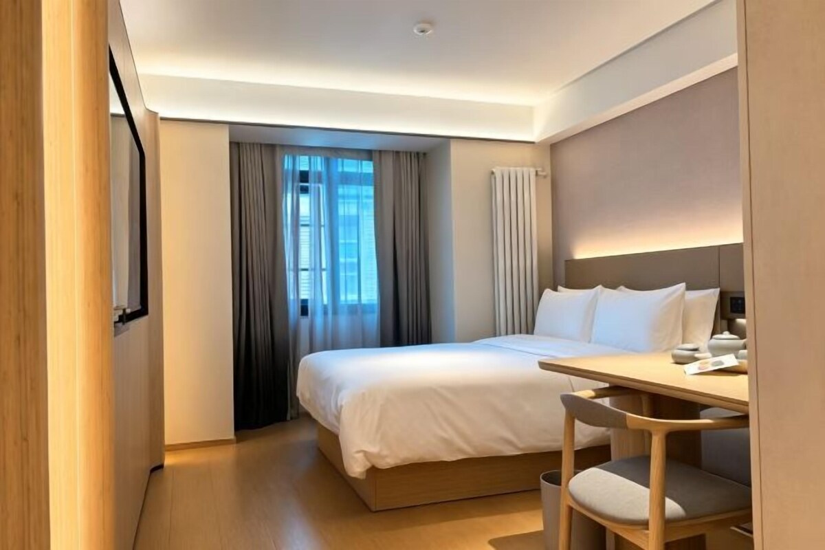 A modern hotel room with a bed, a desk, and a chair.