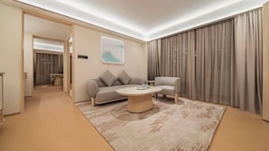 A modern hotel room with a sofa, armchair, and coffee table, a large window with curtains, and a hallway leading to another room. - Ji Hotel (Xi'an High-Tech Zone Tangyan Road) (Xi'an)