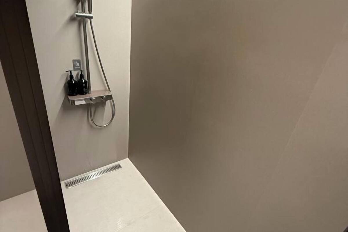 Un bany amb dutxa, prestatges amb productes de tocador i un ventilador.