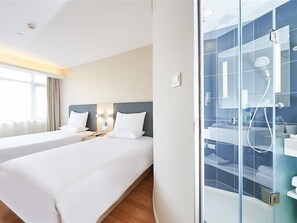 A hotel room with two beds, a glass shower enclosure, and a view of the outdoors.