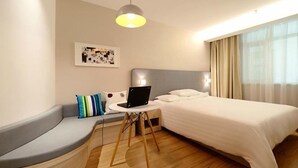 A modern hotel room with a curved seating area, a bed with white linens, a laptop on a small table, and a ceiling light. - Hanting Hotel (Shanghai)