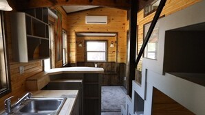 A compact kitchen with wooden walls, a central island, and two sinks. - Secluded Wooded Charmant Chalet  "Theme"  Tiny Home - Off Grid (Aylette)