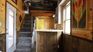 A wooden interior with a staircase, a yellow door, and a bar area. - Secluded Wooded Charmant Chalet  "Theme"  Tiny Home - Off Grid (Aylette)