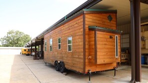 A wooden mobile home with a green roof, a small porch, and a trailer attached. - Secluded Wooded Charmant Chalet  "Theme"  Tiny Home - Off Grid (Aylette)