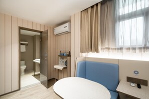 Et hotelværelse med badeværelse, seng, natbord og et vindue med gardiner.
