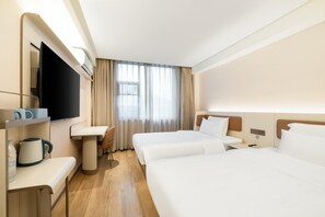 Et hotelværelse med to senge, et skrivebord, en stol, et fjernsyn og et vindue med gardiner.