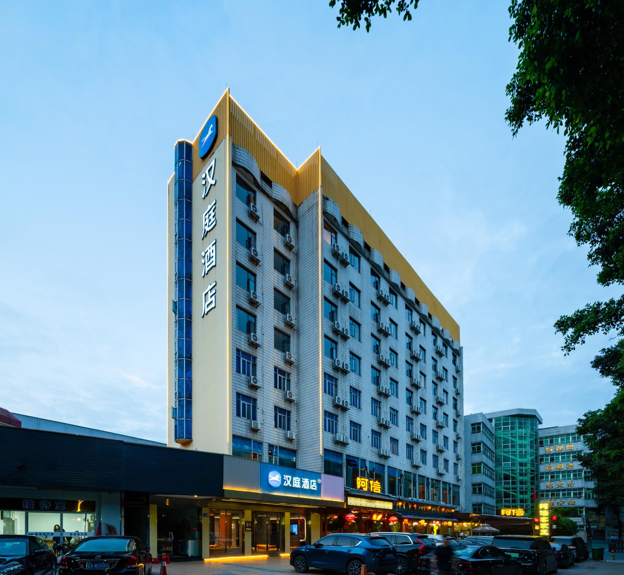Een hotel met meerdere verdiepingen, een opvallend bord op de gevel, tal van ramen en een parkeerplaats met auto's.