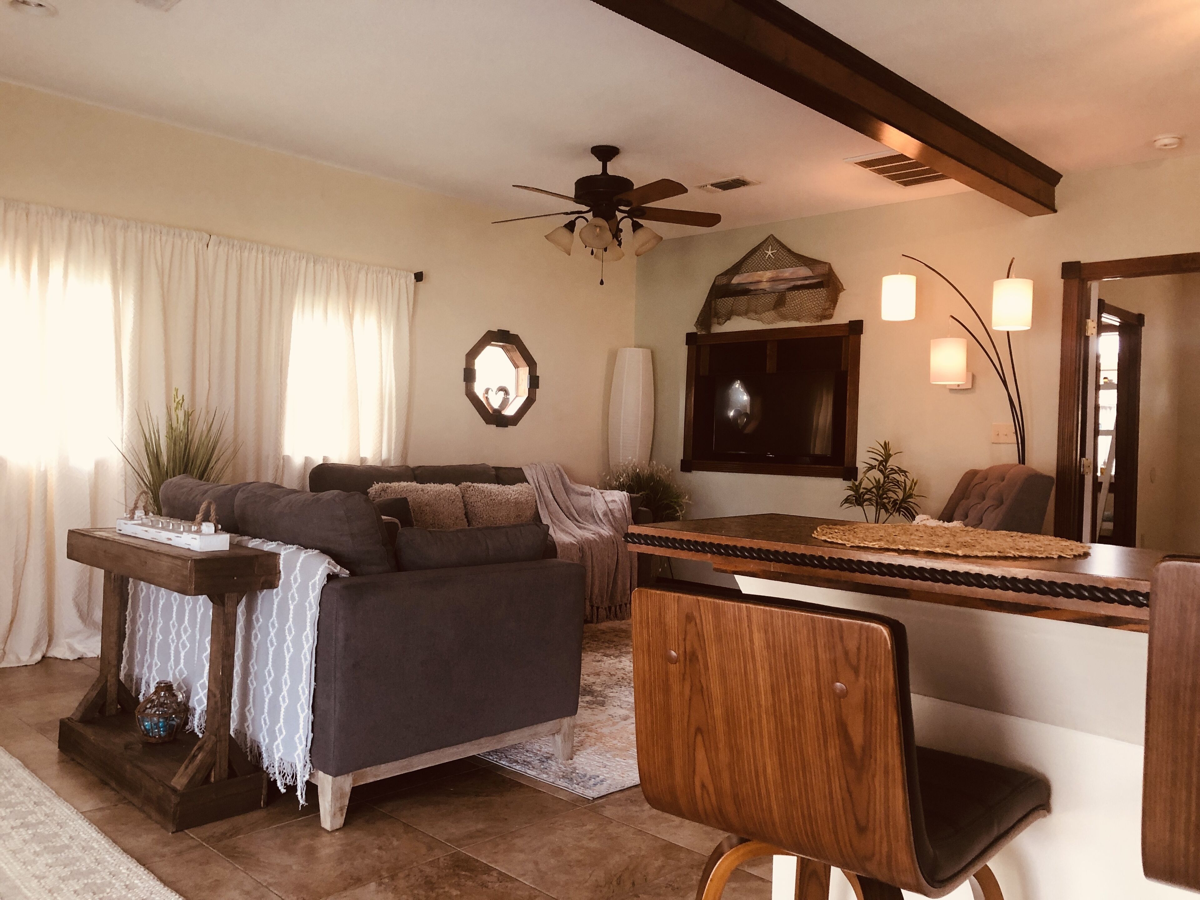A living room with a sofa, a wooden coffee table, a ceiling fan, and a TV mounted on the wall.